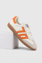A single low-top Back 70 sneaker shown at an angle, resting on a white display block against a light gray studio background. The shoe has an off-white leather upper with bright orange side stripes and heel tab, white laces, a tan gum sole, and a small blue-and-white tongue label.